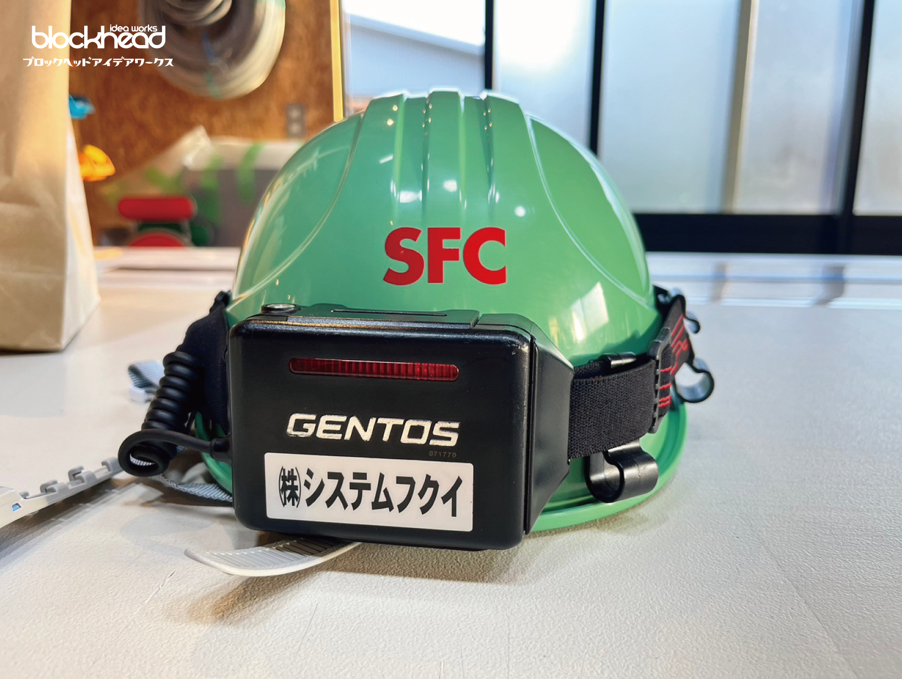 ミントグリーンのヘルメット背面,赤い会社名の英略ロゴ
